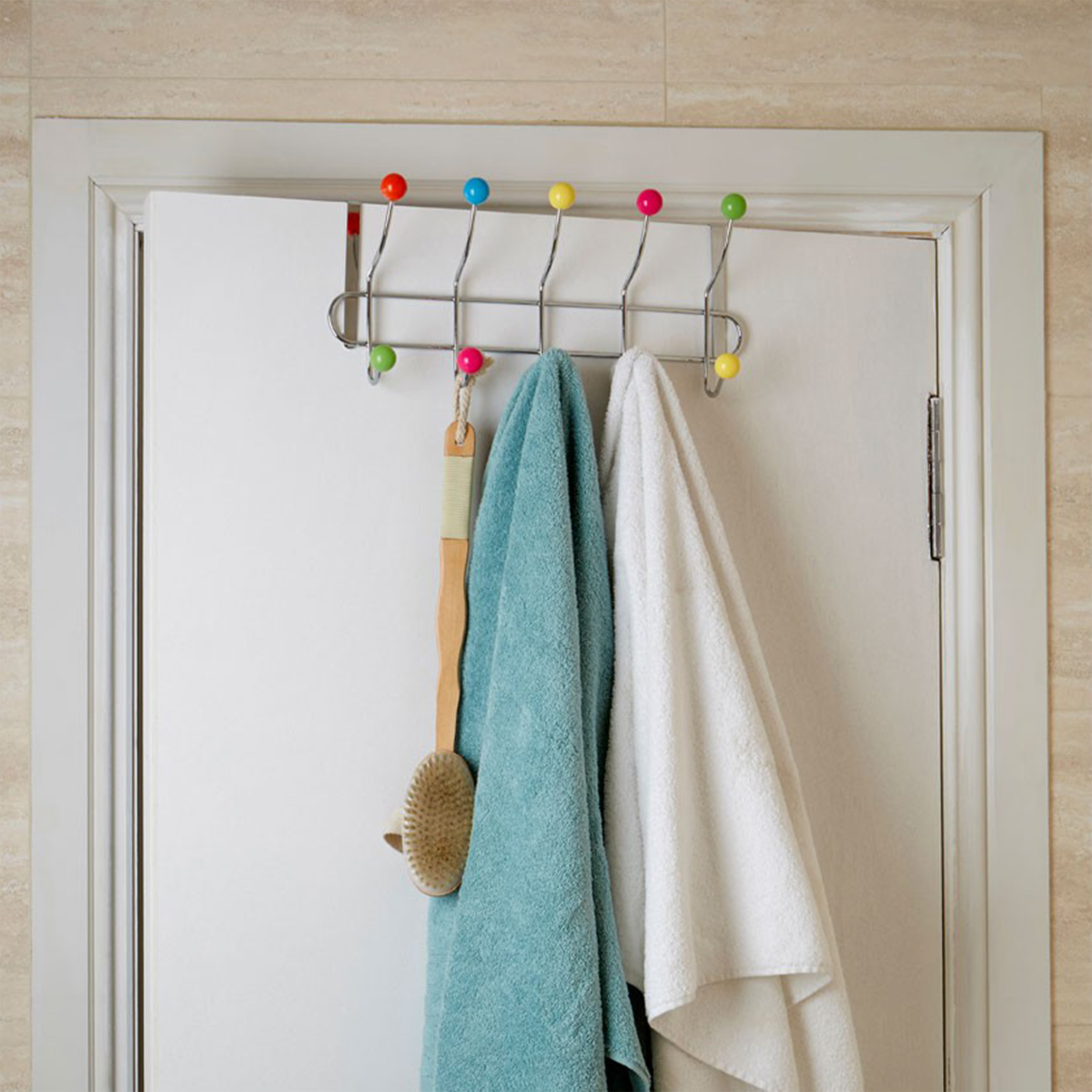 Metal wall hook with colorful knobs holding towels and a brush against a white door.