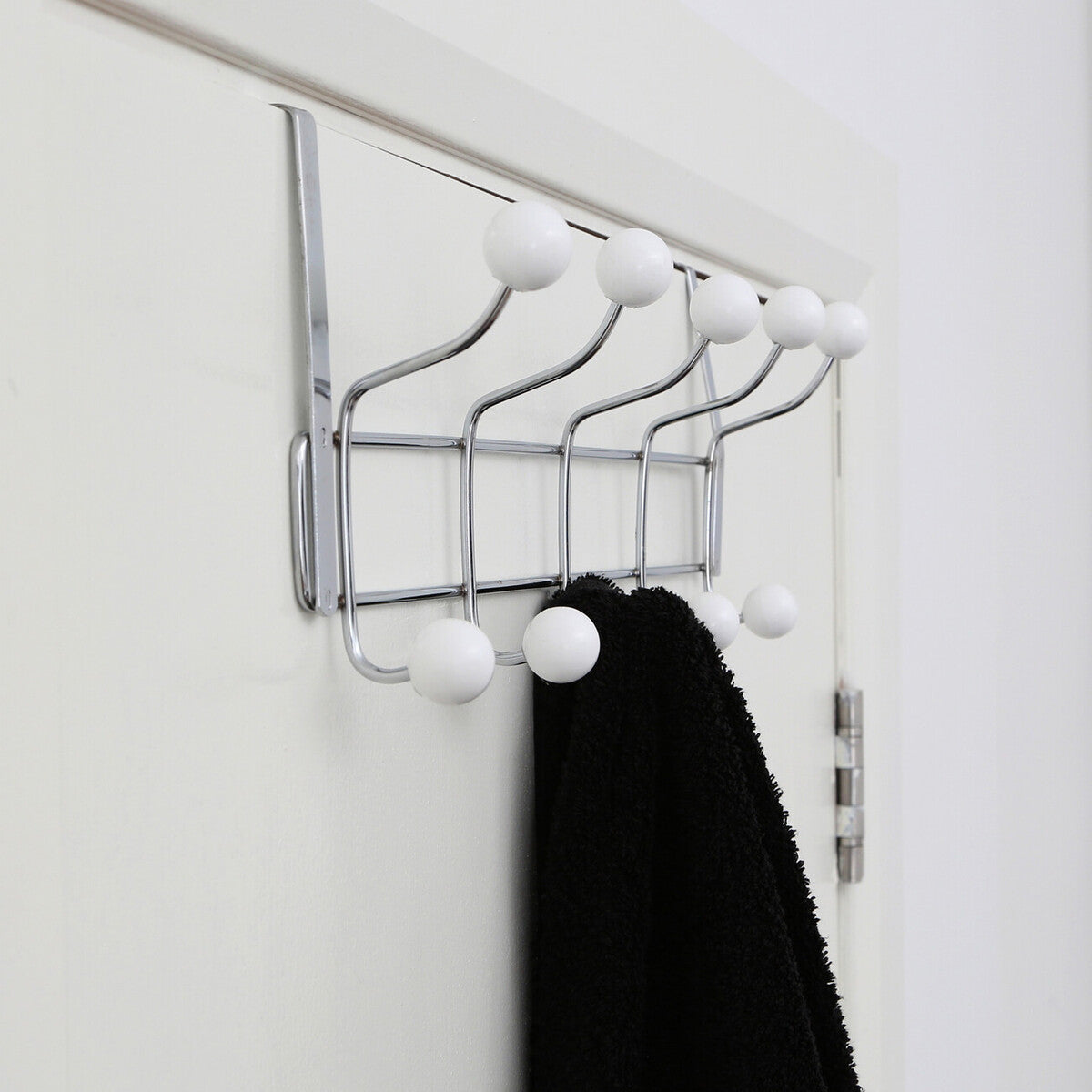 Metal wall hook with white hooks holding a black towel on a white wall.