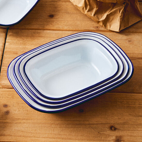 Set of white enameled dishes with blue rims on a wooden surface, accompanied by eggs in a paper bag.