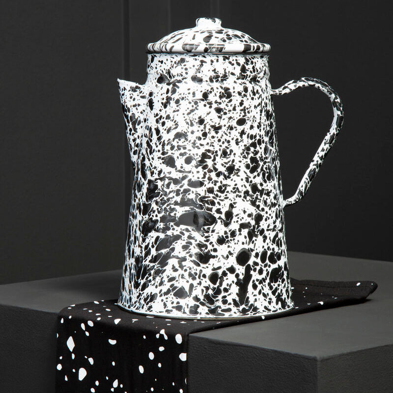 Speckled black and white coffee pot on a dark surface with a black background