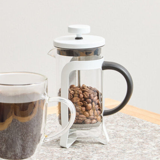 Clear glass mug with coffee and French press on a wooden surface