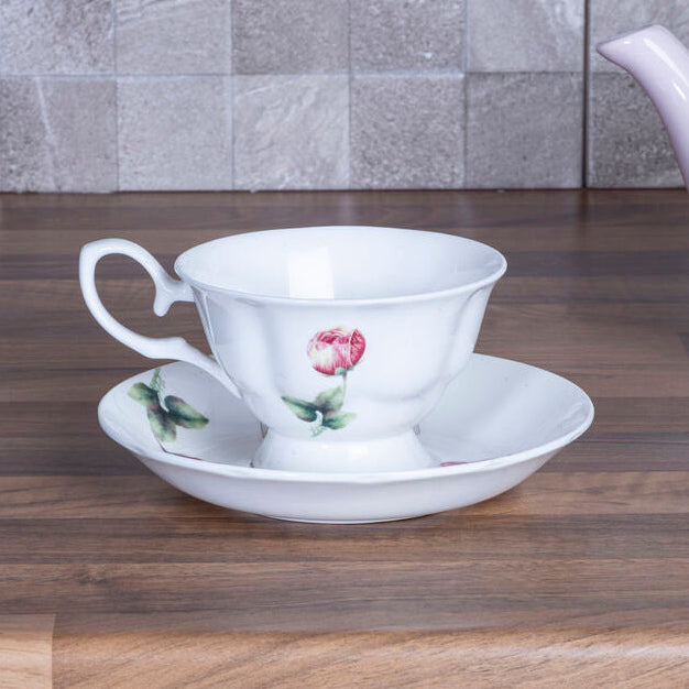 Ceramic teacup with floral design on a saucer next to a teapot on a wooden surface.