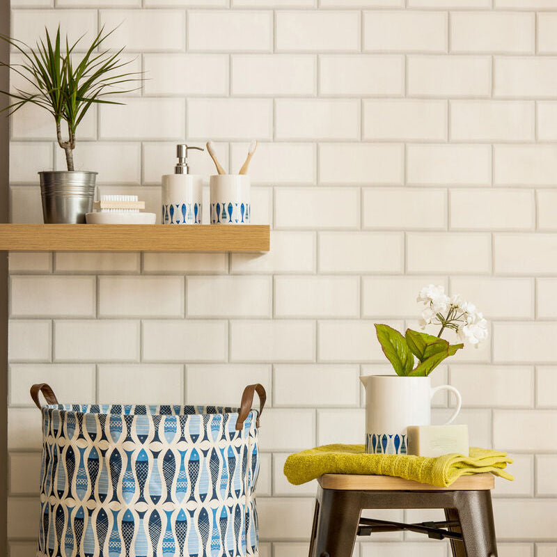 Patterned laundry basket next to a wooden stool with a green towel on a tiled wall background