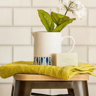 Patterned laundry basket next to a wooden stool with a green towel on a tiled wall background