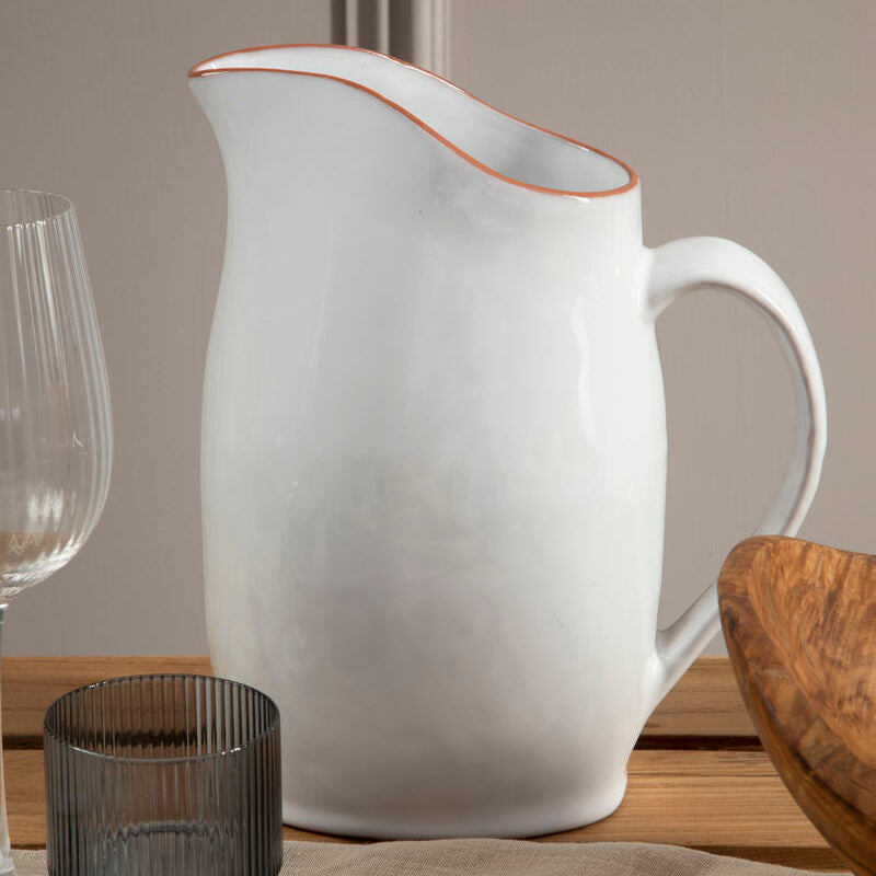 White ceramic pitcher on a wooden table with glasses and a bowl.