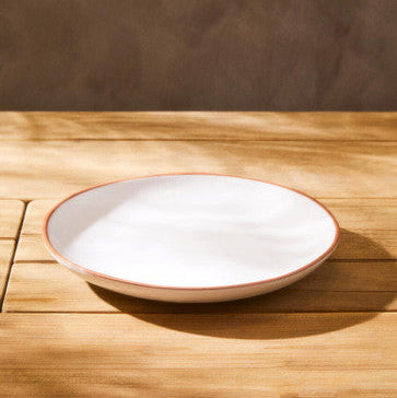 White ceramic plate with a red rim on a wooden surface