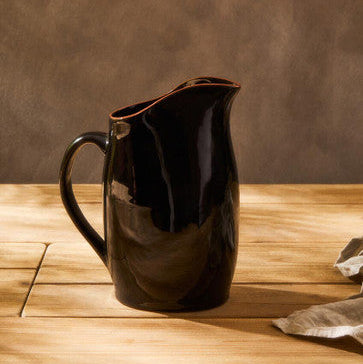Black ceramic pitcher on a wooden surface with a brown background