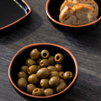 Bowl of green olives on a dark wooden surface with another bowl in the background.