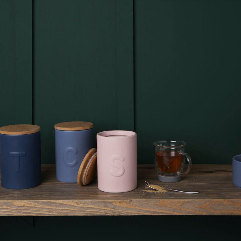 Set of ceramic containers and a glass mug on a wooden surface with a dark green wall background.