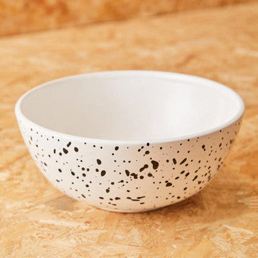 White ceramic bowl with black speckles on a beige surface