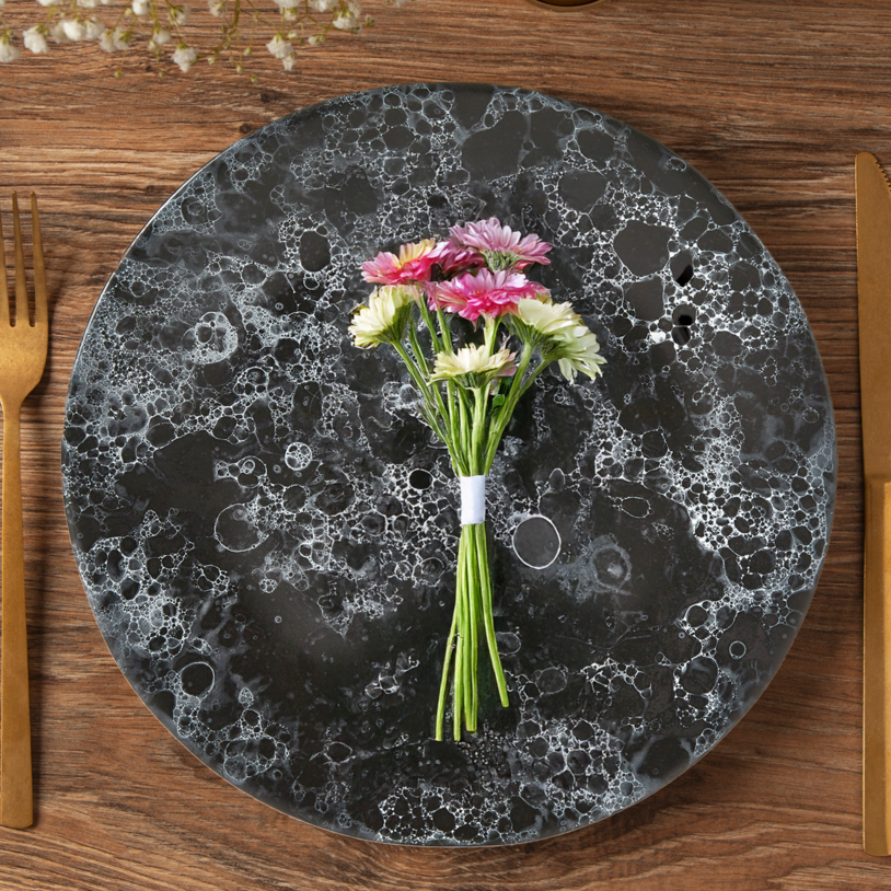 Dining table setting with marble effect plate, gold cutlery, and flowers on a wooden surface.