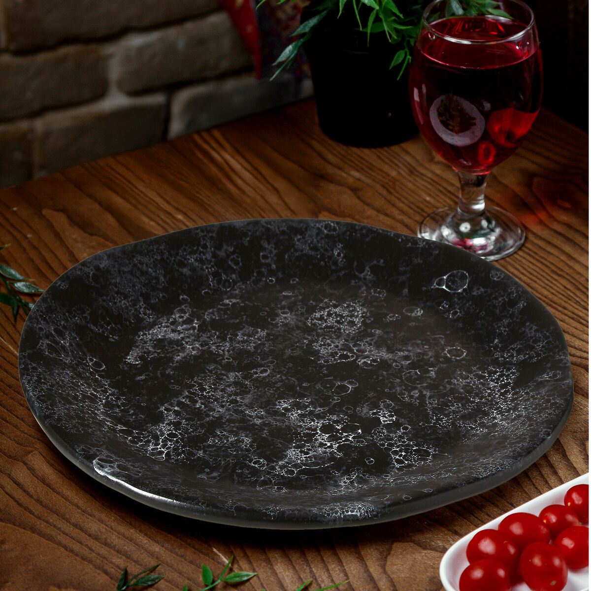 Black textured plate on a wooden table with a glass of red wine and cherry tomatoes.