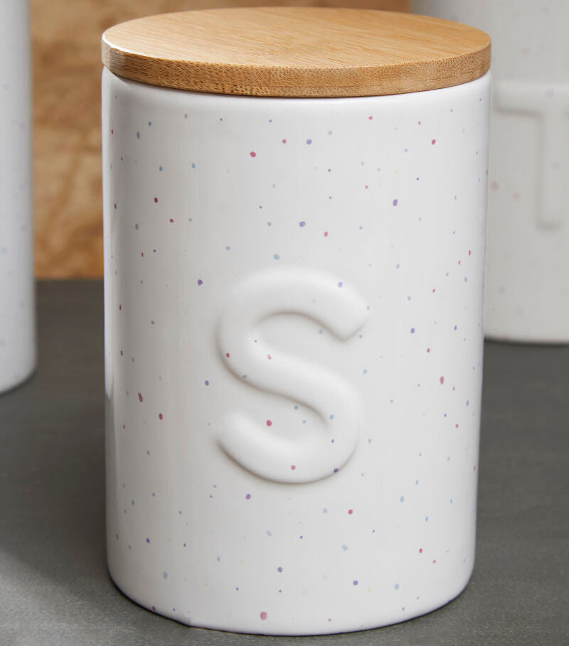 White speckled ceramic jar with a wooden lid on a gray surface.