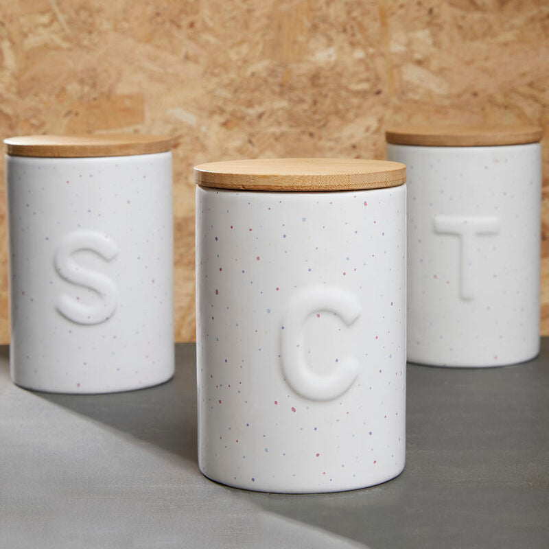 Three white ceramic canisters with wooden lids on a wooden background
