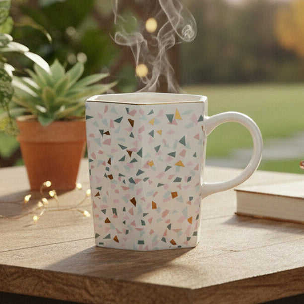 Steaming mug on a wooden table with plants and a book in the background, featuring the brand &