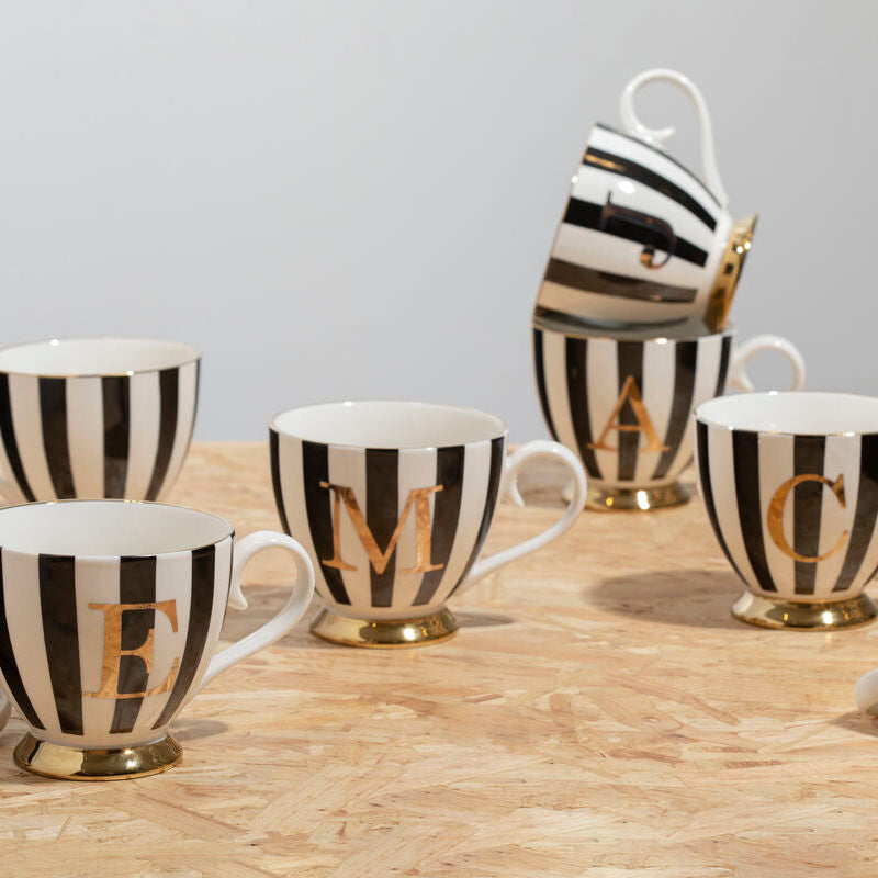 Set of black and white striped mugs with gold lettering on a wooden surface.