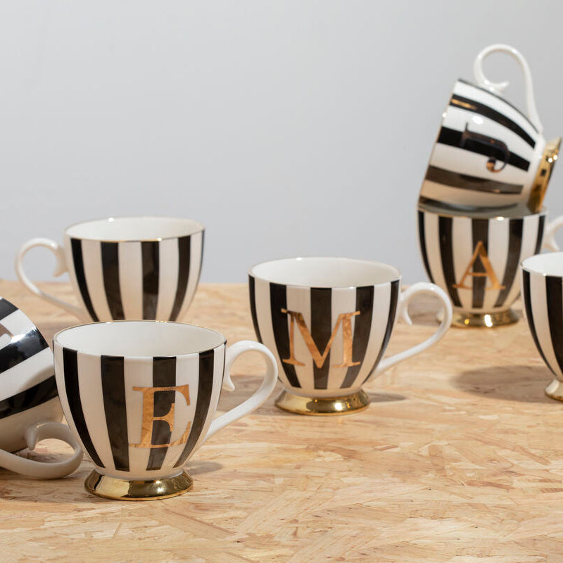 Set of black and white striped mugs with gold lettering on a wooden surface.