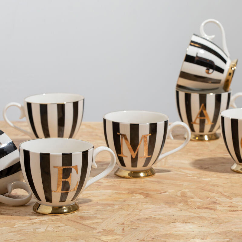 Set of black and white striped mugs with gold lettering on a wooden surface.