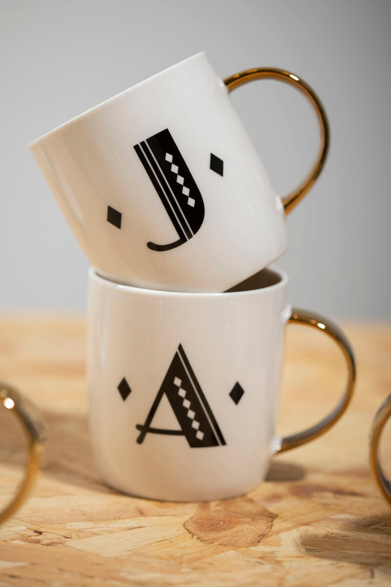 Two white mugs with black letter designs stacked on a wooden surface.