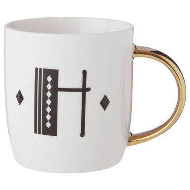 White mug with gold handle and black geometric design on a white background