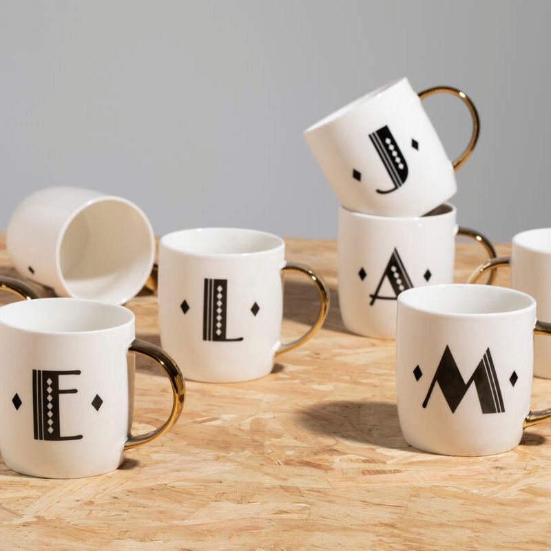 Set of white mugs with black letter designs on a wooden surface