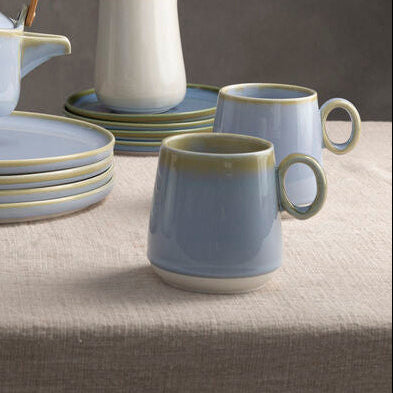 Ceramic tableware set on a neutral background with a hand reaching for a teapot.