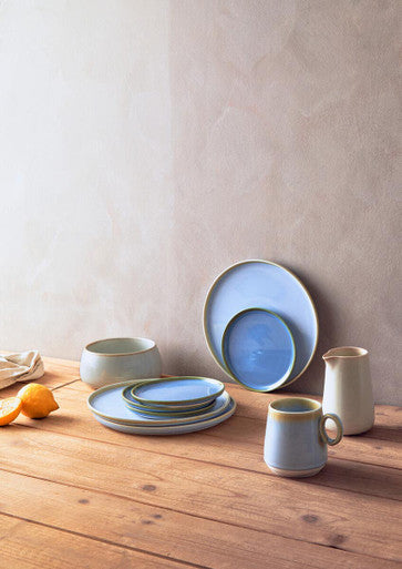 Set of blue ceramic dishes and mugs on a wooden surface with a neutral background