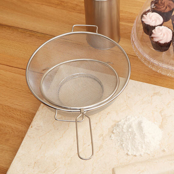 Metal strainer on a kitchen counter with cupcakes in the background