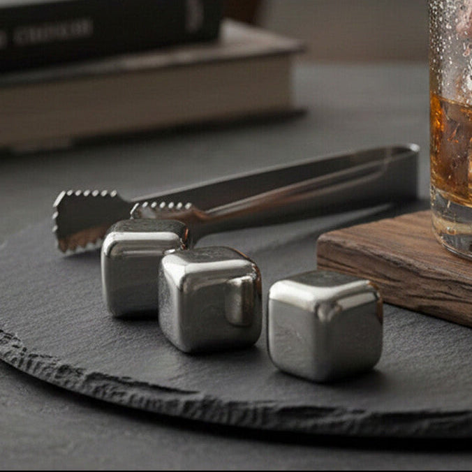 Glass of whiskey with ice cubes on a coaster, surrounded by whiskey stones and a book in a cozy room.