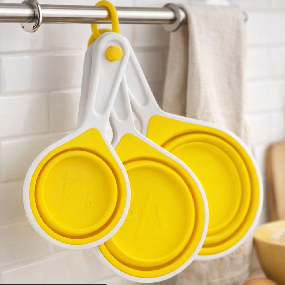 Yellow and white collapsible measuring cups hanging on a rack with kitchen items in the background.