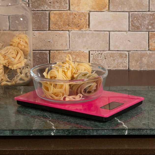 Clear glass bowl with pasta on a pink digital scale against a stone wall background
