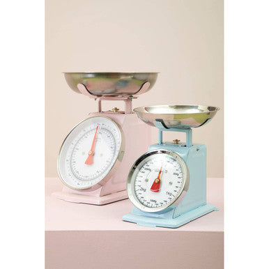 Two vintage-style kitchen scales, one pink and one blue, on a light pink background.