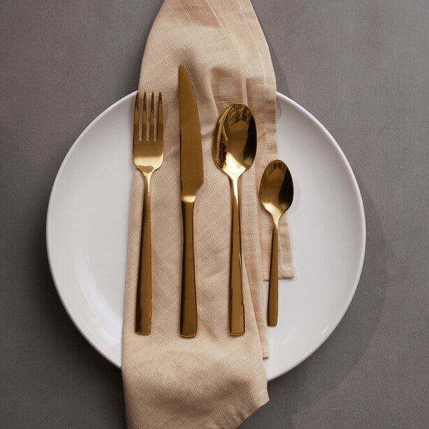 Gold cutlery set on a white plate with a beige napkin against a gray background