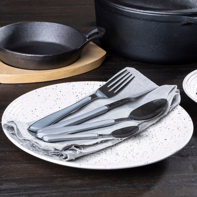 Black cast iron cookware and silver cutlery on a speckled plate.