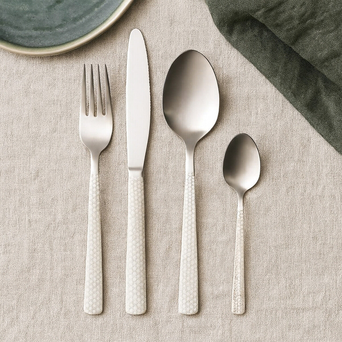 Set of silver cutlery including fork, knife, and two spoons on a textured surface.