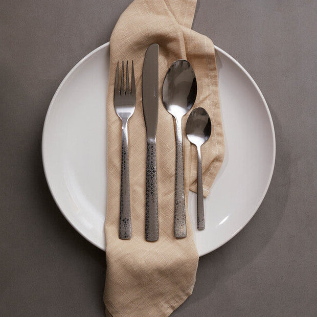 Silverware set on a white plate with a beige napkin against a dark background