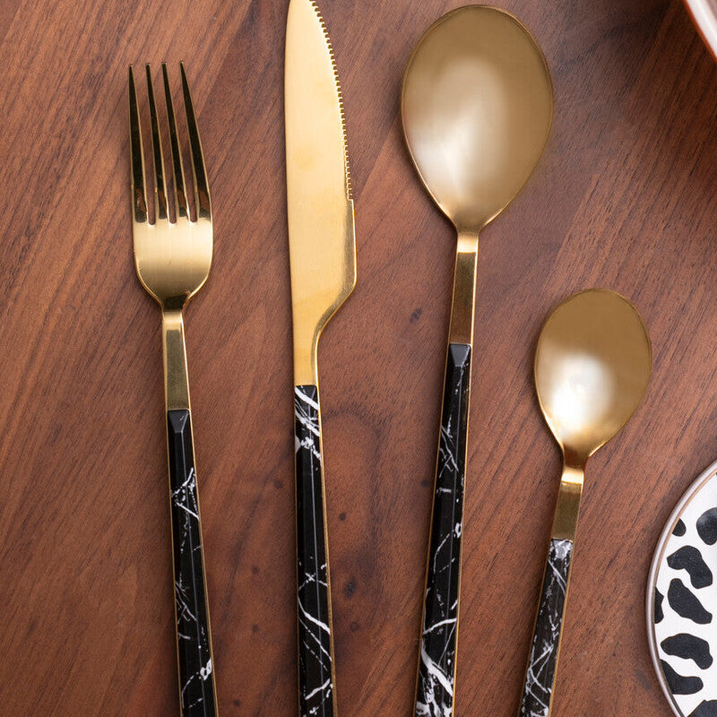 Set of gold and black marble-patterned cutlery on a wooden surface