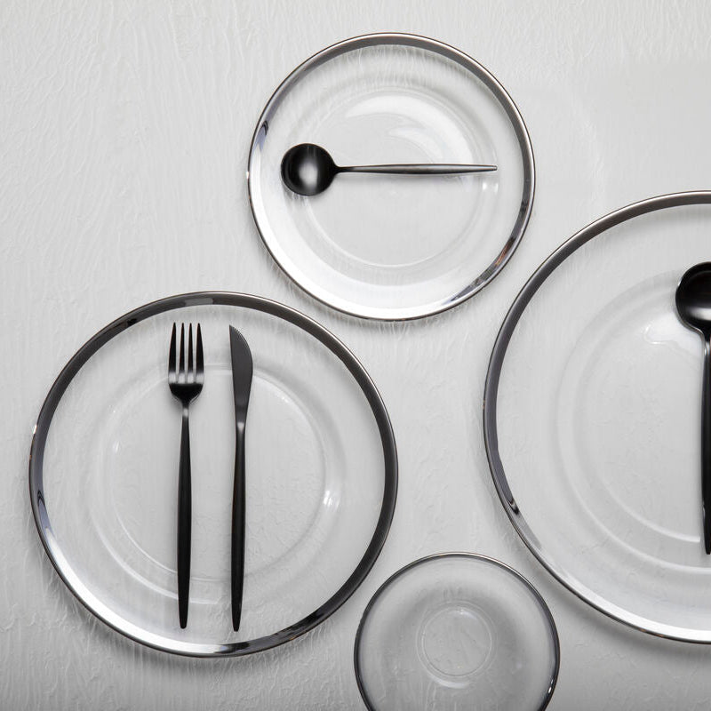 Set of clear glass plates with black cutlery on a light gray background