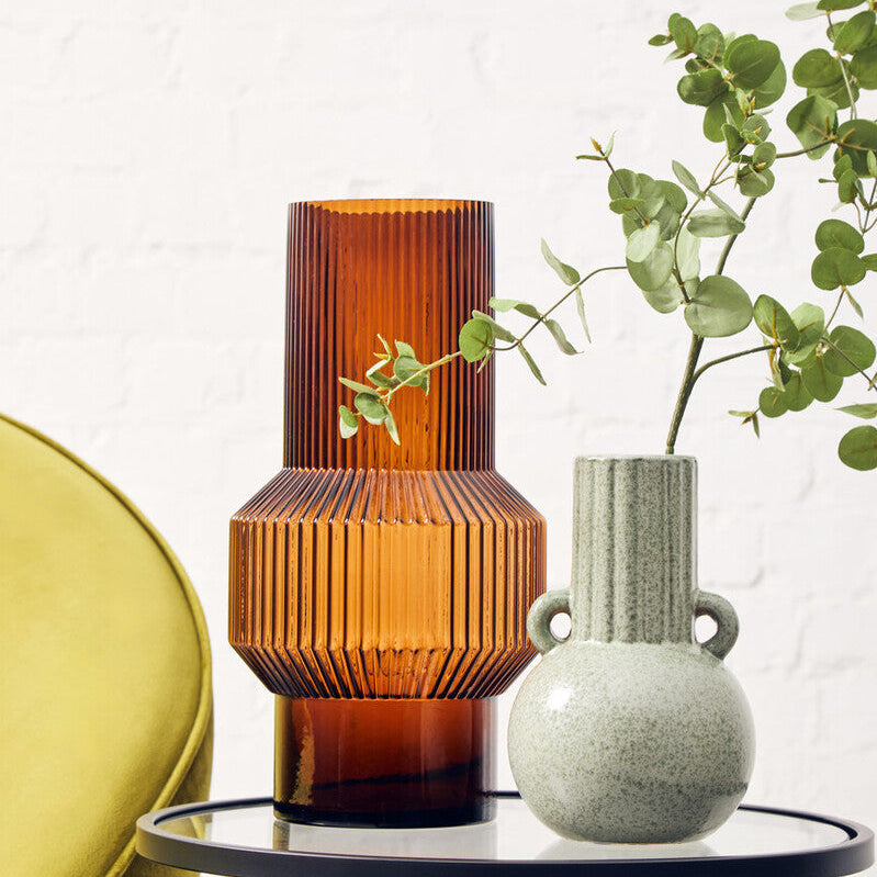 Two vases on a small round table with a plant in the background