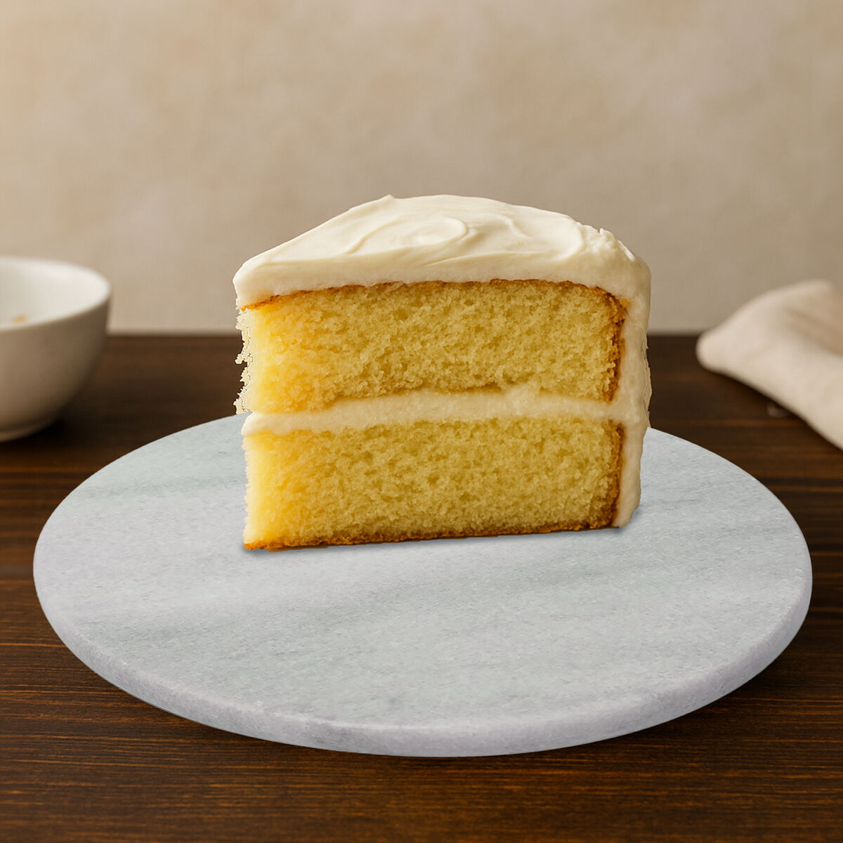 Slice of yellow cake with white frosting on a marble coaster