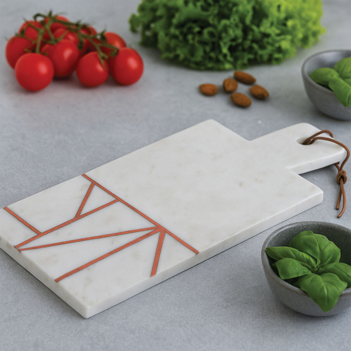 Marble cutting board with geometric design on a kitchen counter with vegetables.