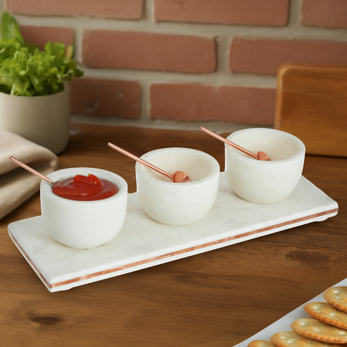 Three small white bowls with dipping sauces on a marble tray against a brick wall.