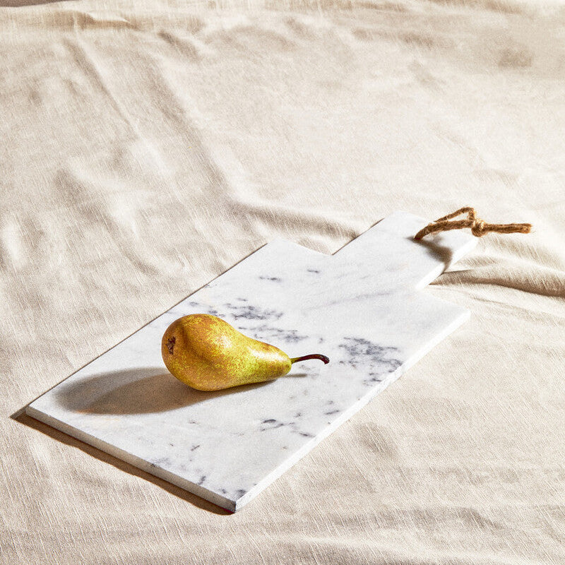 Pear on a marble slab with a gold knife on a beige fabric background