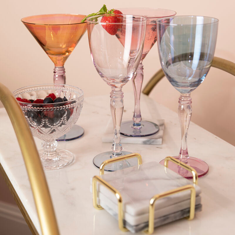 Set of colorful glassware on a marble surface with a gold holder.