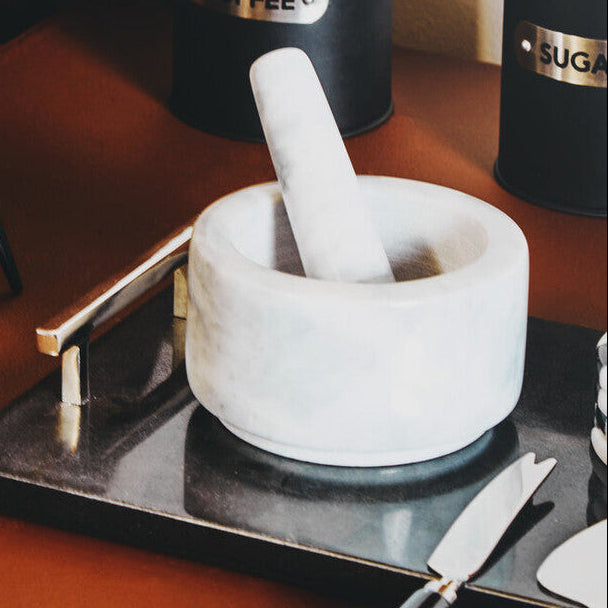 Mortar and pestle on a wooden surface with coffee and sugar containers in the background.