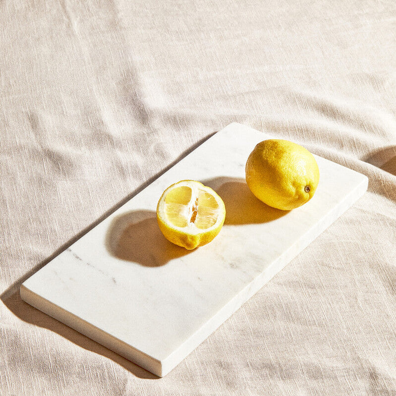 Two lemons on a white cutting board with a beige cloth background
