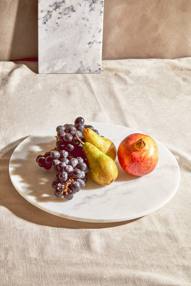 Fruits including grapes, pears, and a pomegranate on a marble plate with a marble background.