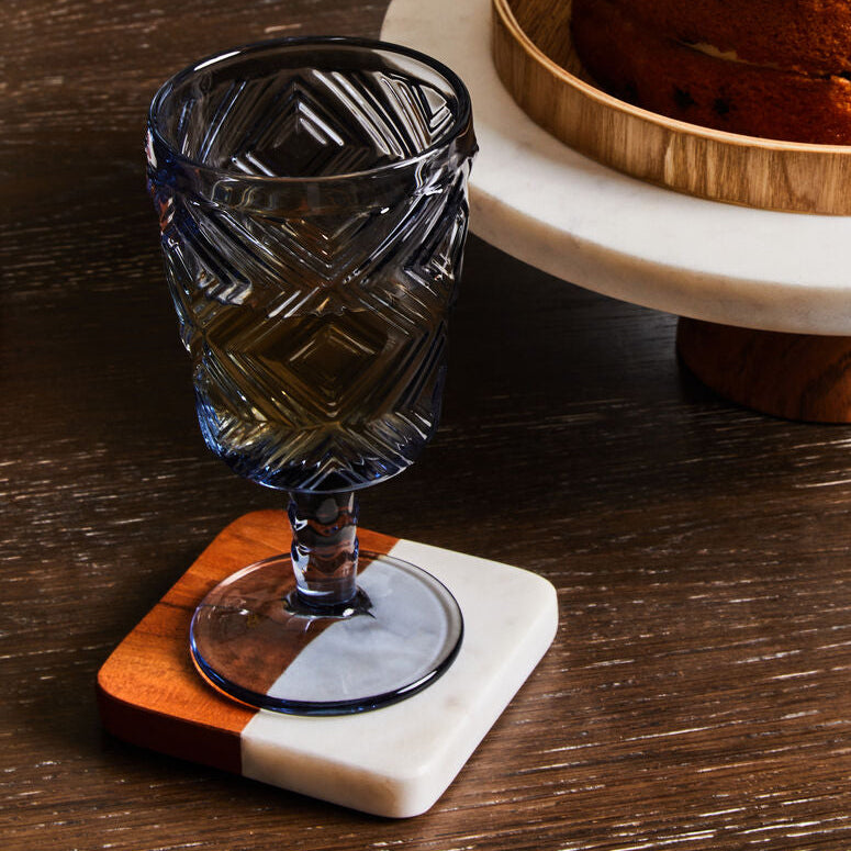 Glass with a coaster on a wooden table next to a cake on a marble stand.