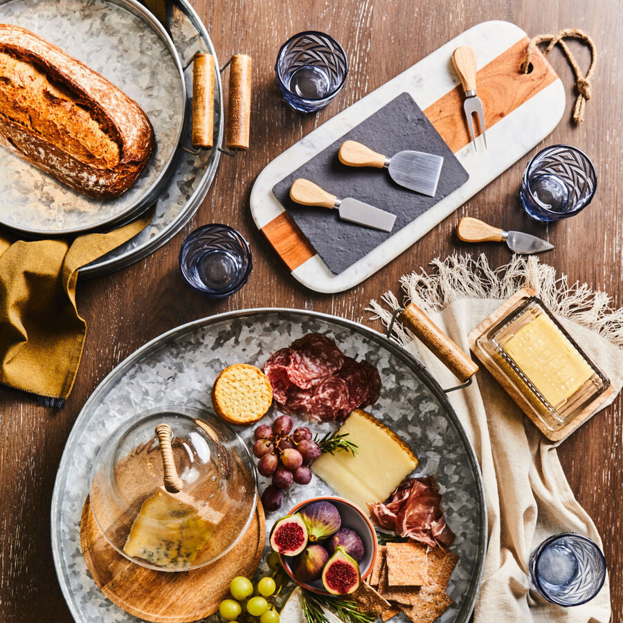 Platter of assorted cheeses, fruits, and meats with glasses on a wooden table.