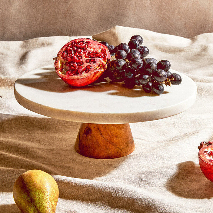 Fruits including pomegranates and grapes on a marble stand with a beige background